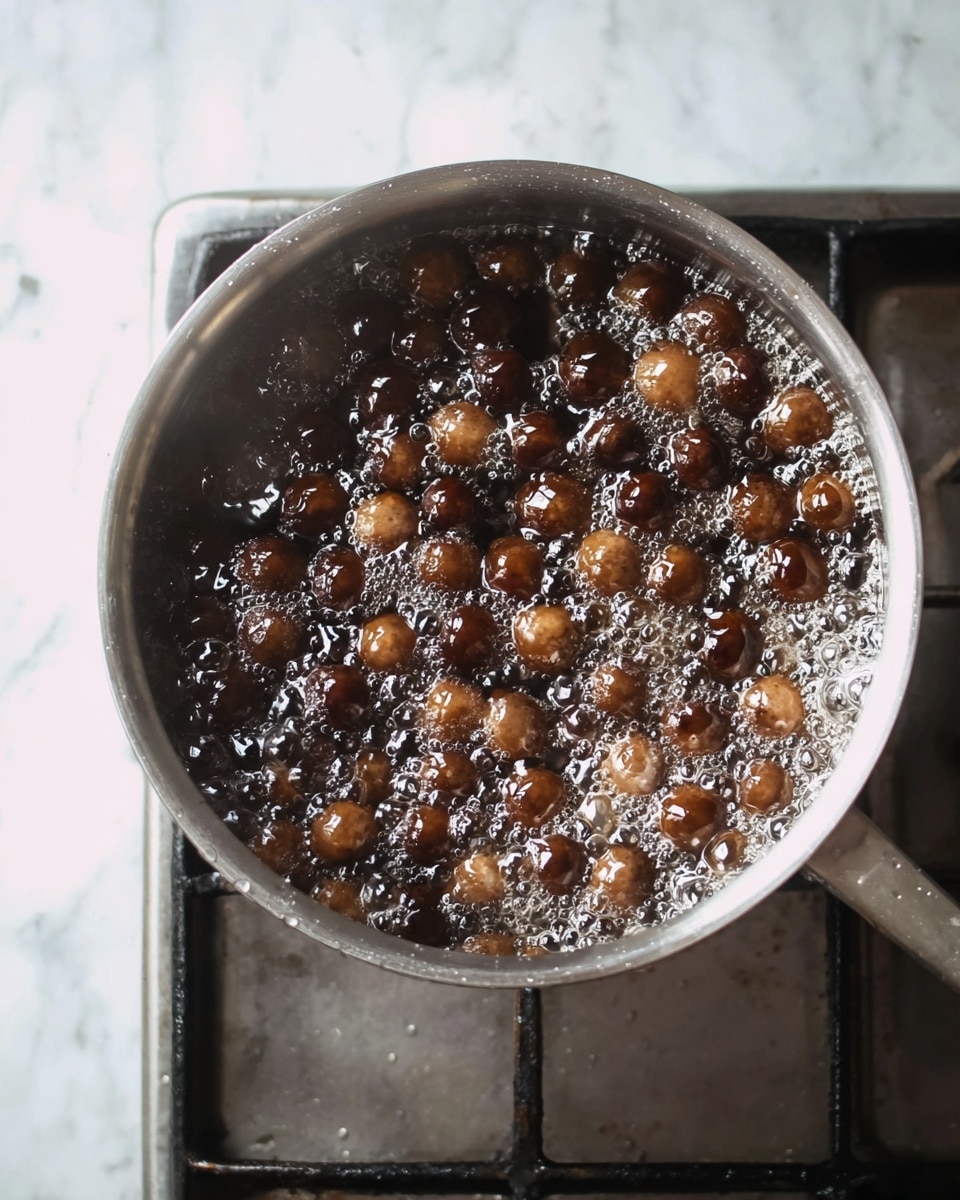 A silver pot filled with boiling water contains many small, round, dark brown balls that are bubbling actively with foam on the surface. The pot sits on a metal stove burner, and the background is a white marbled texture. The dark brown spheres float and move in the clear bubbling water, showing different shades of brown from light to dark under the steam. photo taken with an iphone --ar 4:5 --v 7
