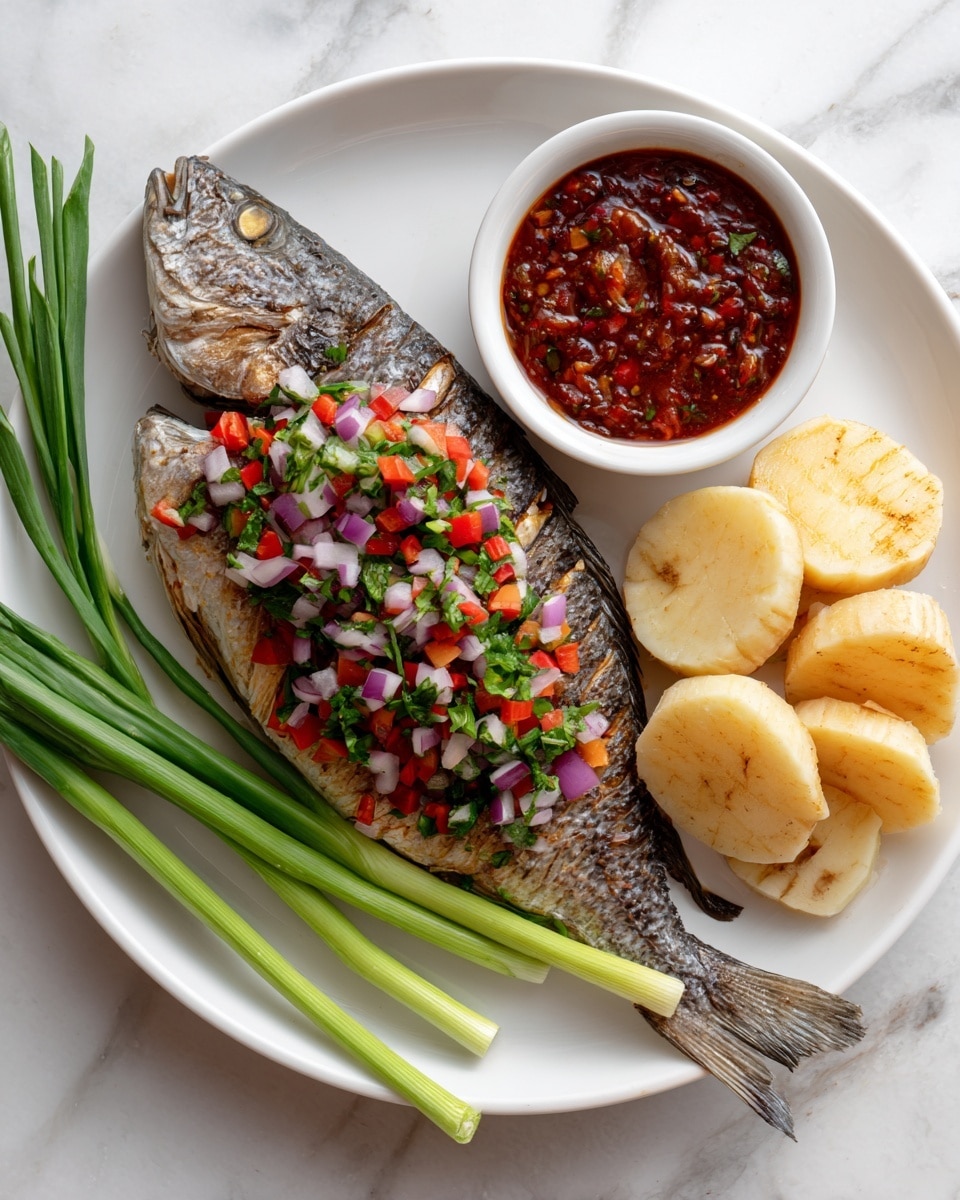 A whole grilled fish with dark brown, crispy skin covered in herbs and spices lies at the center of a white plate. On the top left side of the fish, there is a colorful mixture of finely chopped red onions, red tomatoes, and green herbs. To the right of the fish, sliced white yams are arranged neatly near a small white bowl filled with thick, reddish-brown sauce. At the bottom left of the fish, two fresh, bright green stalks of scallions rest on the plate. The plate sits on a white marbled surface. Photo taken with an iphone --ar 4:5 --v 7