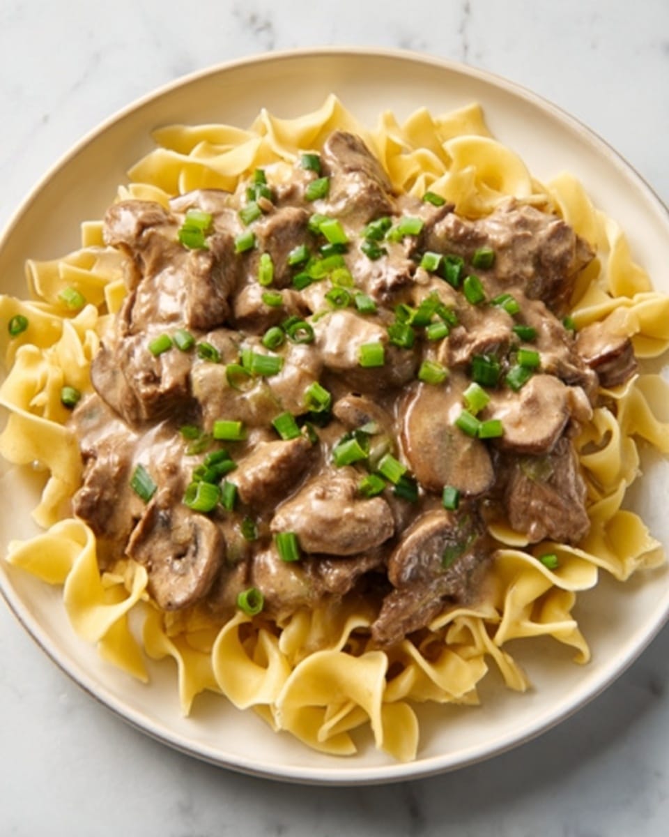 A white bowl filled with a base layer of curly, light yellow pasta noodles. On top, there is a thick layer of creamy brown sauce mixed with small chunks of cooked meat. Scattered green chopped scallions are sprinkled over the meat and sauce, adding a splash of color. The background shows a white marbled surface. photo taken with an iphone --ar 4:5 --v 7