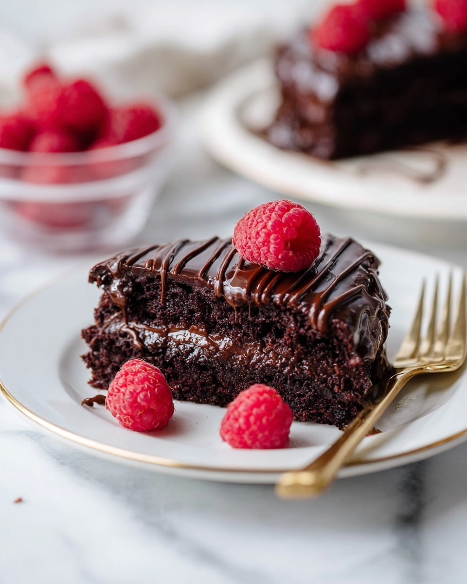 A piece of chocolate cake is placed on a white plate with a thin gold rim. The cake has two layers of dark, moist chocolate with a rich chocolate filling in the middle. On top, glossy dark chocolate drizzle runs in lines across the surface. Three bright red raspberries sit on the cake, and two more raspberries rest on the plate next to the cake. The plate is set on a white marbled surface. In the background, another piece of chocolate cake topped with raspberries and a glass bowl filled with raspberries can be seen softly out of focus. A gold fork lies nearby on the surface. Photo taken with an iphone --ar 4:5 --v 7