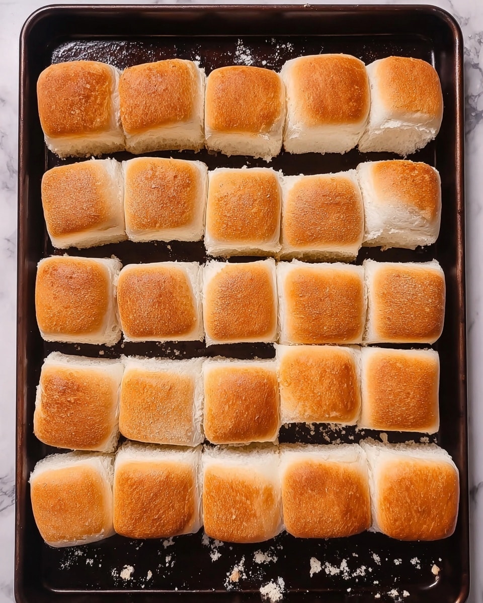 The image shows a baking tray filled with twenty-four square pieces of white bread, arranged in six rows and four columns. Each piece has a golden-brown crust on the top edge and soft, fluffy white interior, with slight crumbs scattered around on the tray. The tray is dark-colored, with some shiny spots reflecting light. The background features a white marbled texture. Photo taken with an iphone --ar 4:5 --v 7