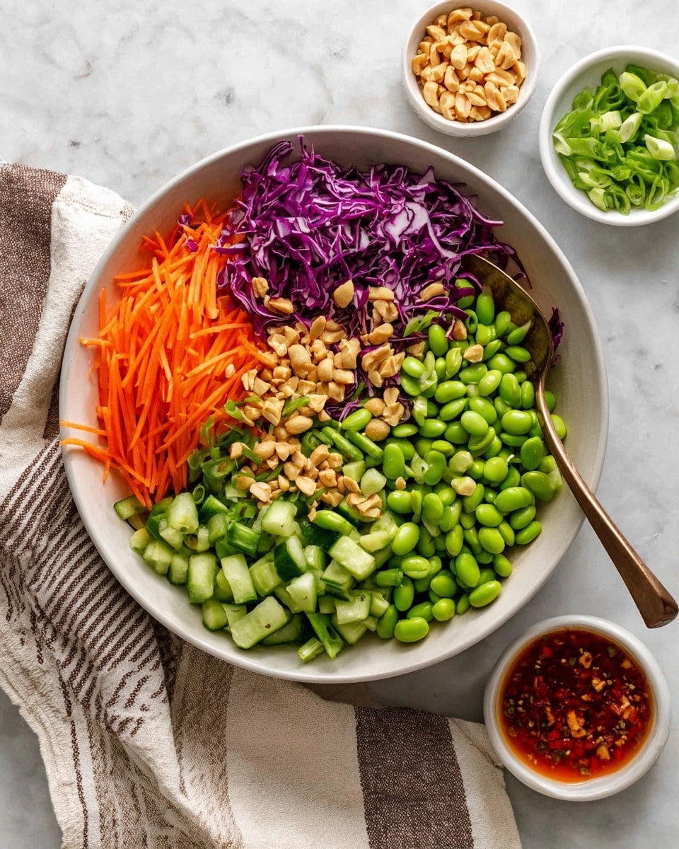 A white bowl filled with colorful chopped vegetables and nuts arranged in sections. Starting clockwise, bright orange thin carrot sticks sit on the left side above dark green cucumber pieces, then a large portion of light green edamame beans fills the lower right, purple cabbage strips are placed above them, and sliced green beans cover the top right. Chopped peanuts are sprinkled in the middle of the bowl. A bronze spoon rests on the edge of the bowl on the left side. On the white marbled surface around the bowl, three small white bowls hold extra chopped peanuts, sliced green beans, and a red sauce with bits inside. A white cloth with a beige and dark brown striped pattern is partially under the bowl on the lower left. Photo taken with an iphone --ar 4:5 --v 7