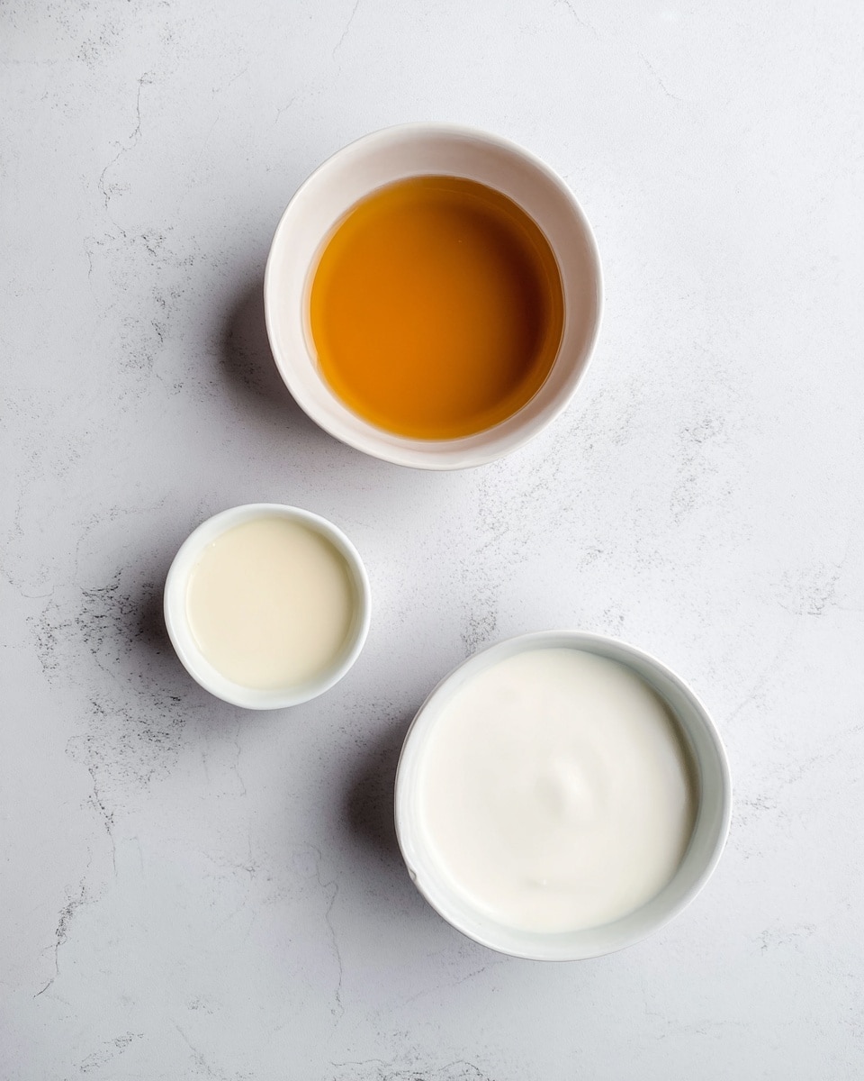 The image shows three small white bowls placed on a white marbled surface. The top bowl contains a golden brown liquid with a smooth texture. Below it, on the left side, is a small bowl filled with a light creamy liquid. At the bottom right, there is a slightly larger bowl holding a white creamy liquid. The arrangement forms a loose triangle with even spaces between the bowls. The image has soft lighting and a clean, simple look. photo taken with an iphone --ar 4:5 --v 7