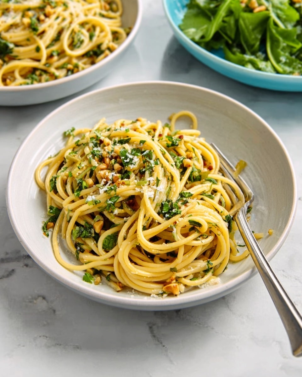 A white bowl filled with a serving of spaghetti pasta mixed with small green herbs and light sauce, the pasta strands look glossy and slightly twisted with some bits of crushed nuts or seeds sprinkled on top. A white marbled surface underneath, with a silver fork next to the bowl, and parts of two other white bowls containing green leafy salad and more spaghetti visible in the background. Photo taken with an iphone --ar 4:5 --v 7