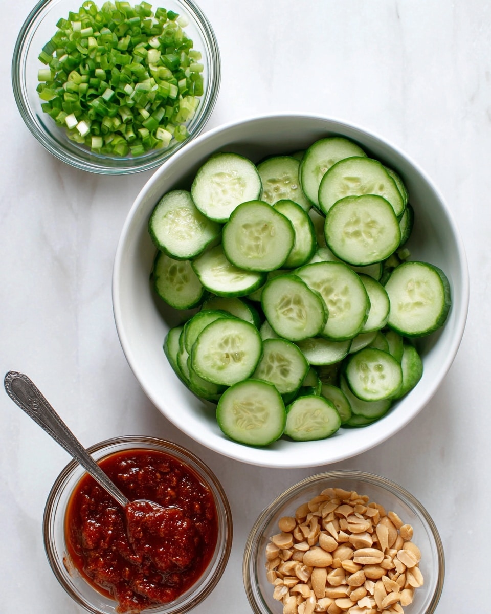 The image shows a top view of four bowls on a white marbled surface. The largest bowl in the center is white and filled with three layers of thick cucumber slices, showing the green skin and pale green inside. Above it to the left is a small clear glass bowl filled with finely chopped green onions in one dense layer. To the right of the onions is a small white bowl filled with three layers of thick, rich red sauce with a spoon resting inside. Below and slightly to the right of the cucumber bowl is a small clear glass bowl filled with small, uneven pieces of light brown crushed peanuts in one layer. Photo taken with an iphone --ar 4:5 --v 7
