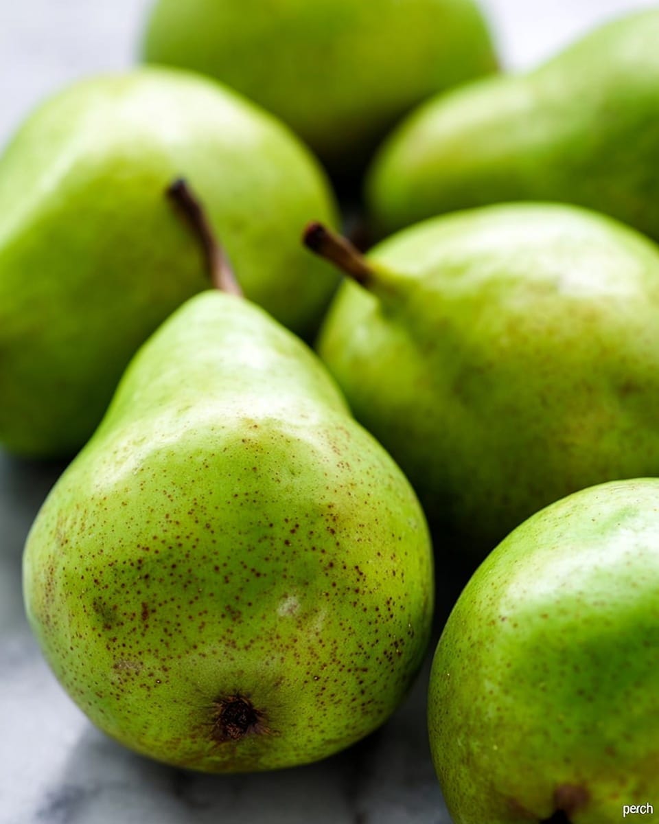 This image shows a close-up of several green pears with a smooth, light green skin covered in small brown specks. The pears have a soft shine, highlighting their fresh texture. They are arranged closely together on a white marbled surface. The pears have short brown stems and vary slightly in size, with some positioned closer to the camera, making them appear larger, while others are farther away. The focus is sharp on the pear in the center, with the other pears softly blurred in the background. photo taken with an iphone --ar 4:5 --v 7