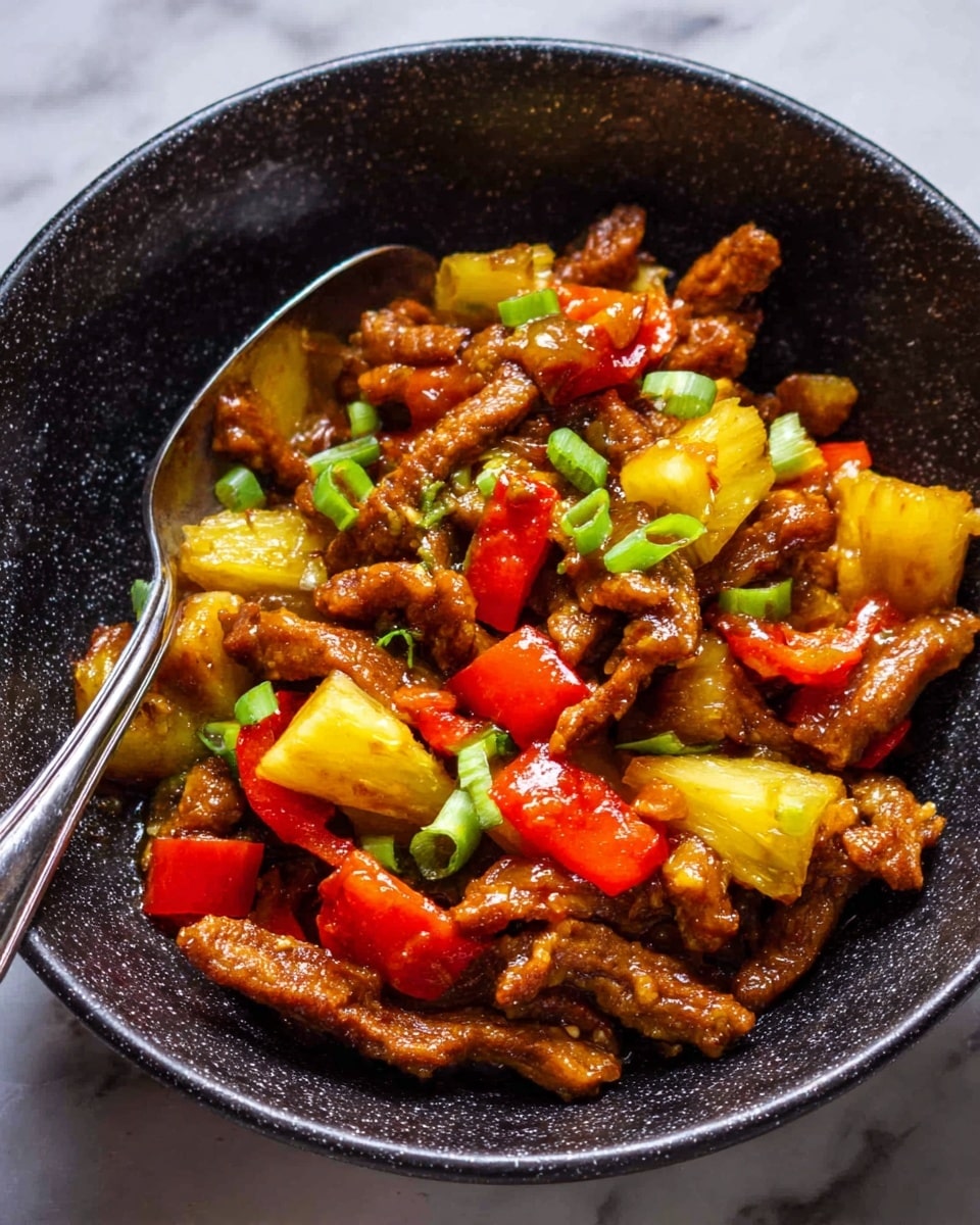 The dish is served in a black speckled bowl filled with multiple pieces of brown cooked strips mixed with yellow pineapple chunks and red bell pepper cubes, garnished with small pieces of green onion on top. A silver metal spoon rests inside the bowl, partially submerged in the food. The bowl sits on a surface with a white marbled texture. The overall look is warm and colorful, with the glossy texture of the food catching light. photo taken with an iphone --ar 4:5 --v 7