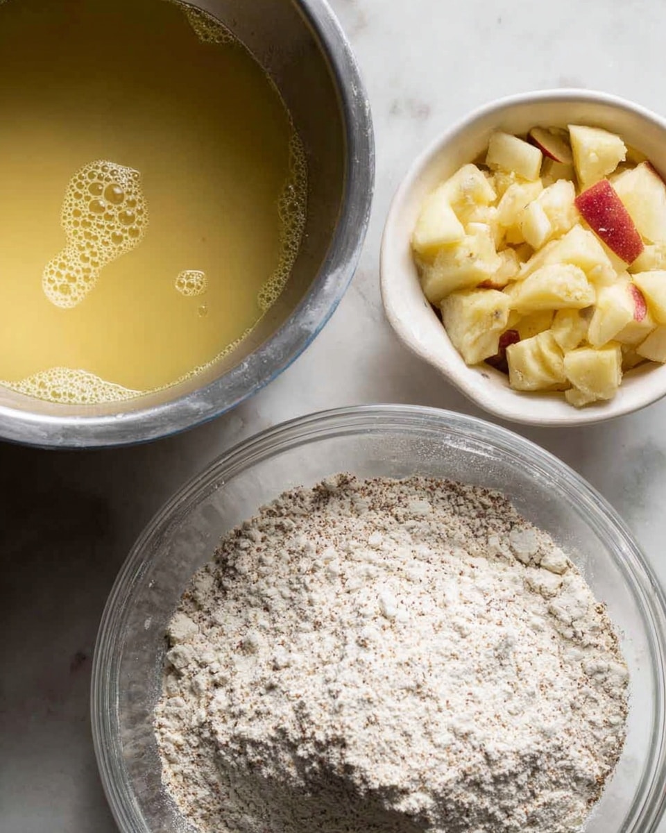 The image shows three containers with ingredients placed on a white marbled surface. In the top left, a silver bowl holds a smooth, yellowish liquid with small bubbles on the surface. At the top right, a white bowl is filled with small, uneven pieces of pale yellow chunks resembling chopped fruit, with one visible piece having red skin. At the bottom, a large transparent bowl contains a mound of flour mixed with finely ground dark specks, with the flour forming a peak and some scattered dust on the sides. The lighting is soft and natural, clearly showing texture and color contrast among the ingredients photo taken with an iphone --ar 4:5 --v 7