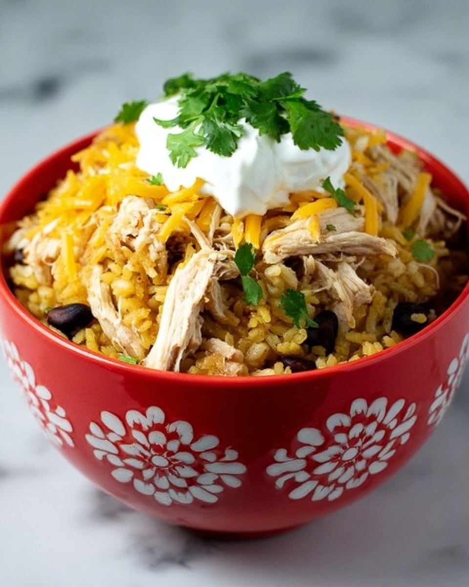 A white bowl filled with a layered dish starting with a base of yellowish rice with small black beans mixed in, topped with shredded light beige chicken pieces. Over the chicken, there is a scattering of shredded yellow cheese and a dollop of white sour cream at the center. Fresh green cilantro leaves are placed on top of the sour cream. A silver spoon is partially dipped into the bowl from the right side. The bowl is placed on a white marbled surface and a white cloth is underneath it. photo taken with an iphone --ar 4:5 --v 7