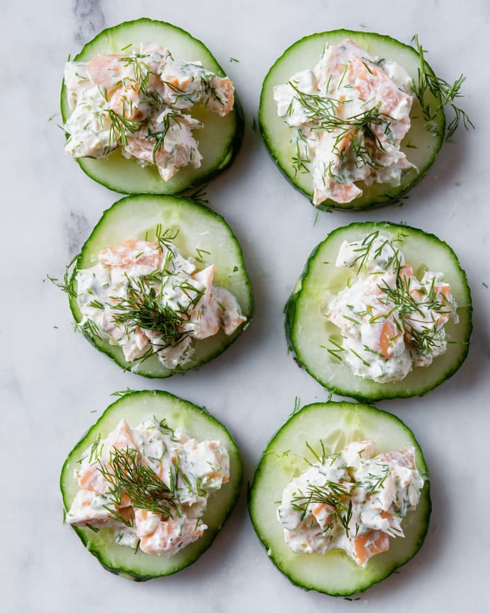Seven cucumber slices lay flat on a white marbled surface, each topped with a creamy mixture of small orange and white chunks mixed in a white sauce. The cucumber slices are light green with darker green edges and moisture visible on the surface. On top of the creamy mixture, tiny sprigs of fresh green dill are scattered evenly, adding a fine texture and fresh color contrast to each piece. The overall look is fresh, simple, and inviting. photo taken with an iphone --ar 4:5 --v 7