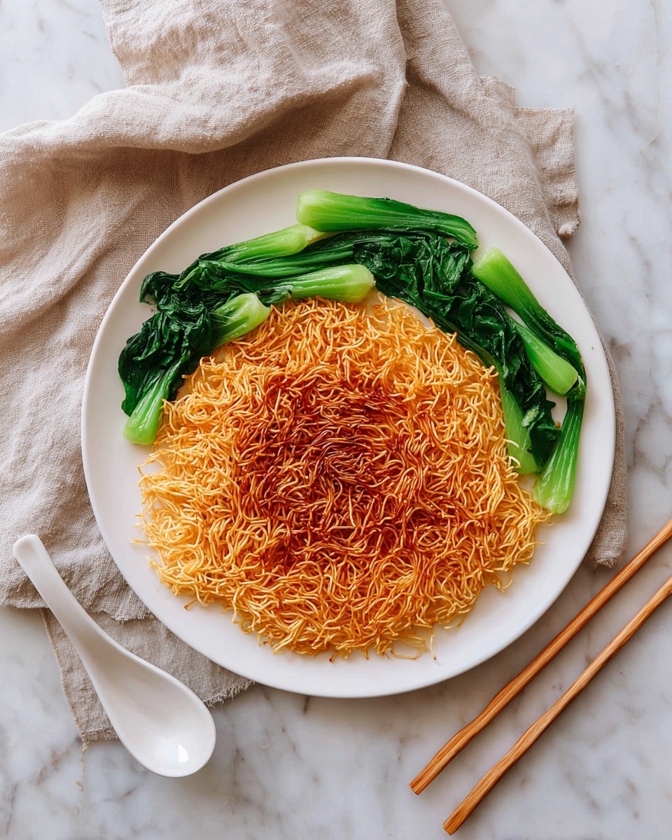 A round white plate holds a single large layer of crispy fried noodles that are golden brown with a slightly darker toasted pattern, covering the whole center of the plate. Around the edges of the noodles, several pieces of bright green cooked leafy vegetables are arranged in groups on opposite sides, adding a fresh contrast. Next to the plate, a pair of light brown wooden chopsticks rests on the white marbled surface, accompanied by a white ceramic soup spoon. The setting also includes a beige linen cloth casually placed nearby. photo taken with an iphone --ar 4:5 --v 7