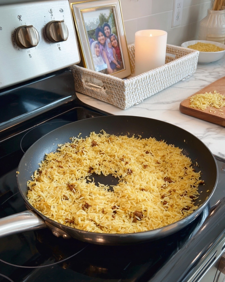 The image shows a lightly toasted yellow rice dish in a large black frying pan on a stovetop with a shiny silver control panel and knobs. The rice is spread evenly across the pan, with a small empty circle in the center where fewer grains are visible. Small bits of browned meat are mixed throughout the rice, adding texture. In the background on a white marbled countertop, there is a white woven tray holding a lit white candle and a framed photo of three children. Next to the tray is a wooden cutting board with some rice grains and a white bowl that has a small amount of rice in it. The whole scene is bright and clean. photo taken with an iphone --ar 4:5 --v 7