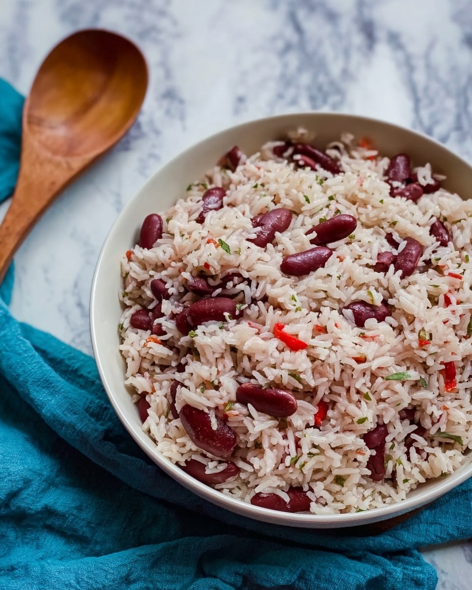 A white bowl filled with a single layer of cooked rice mixed with dark red kidney beans and small pieces of red pepper, showing a soft and slightly moist texture with some herbs visible throughout the mixture. The bowl is placed on a blue cloth next to a wooden spoon on a white marbled surface. photo taken with an iphone --ar 4:5 --v 7