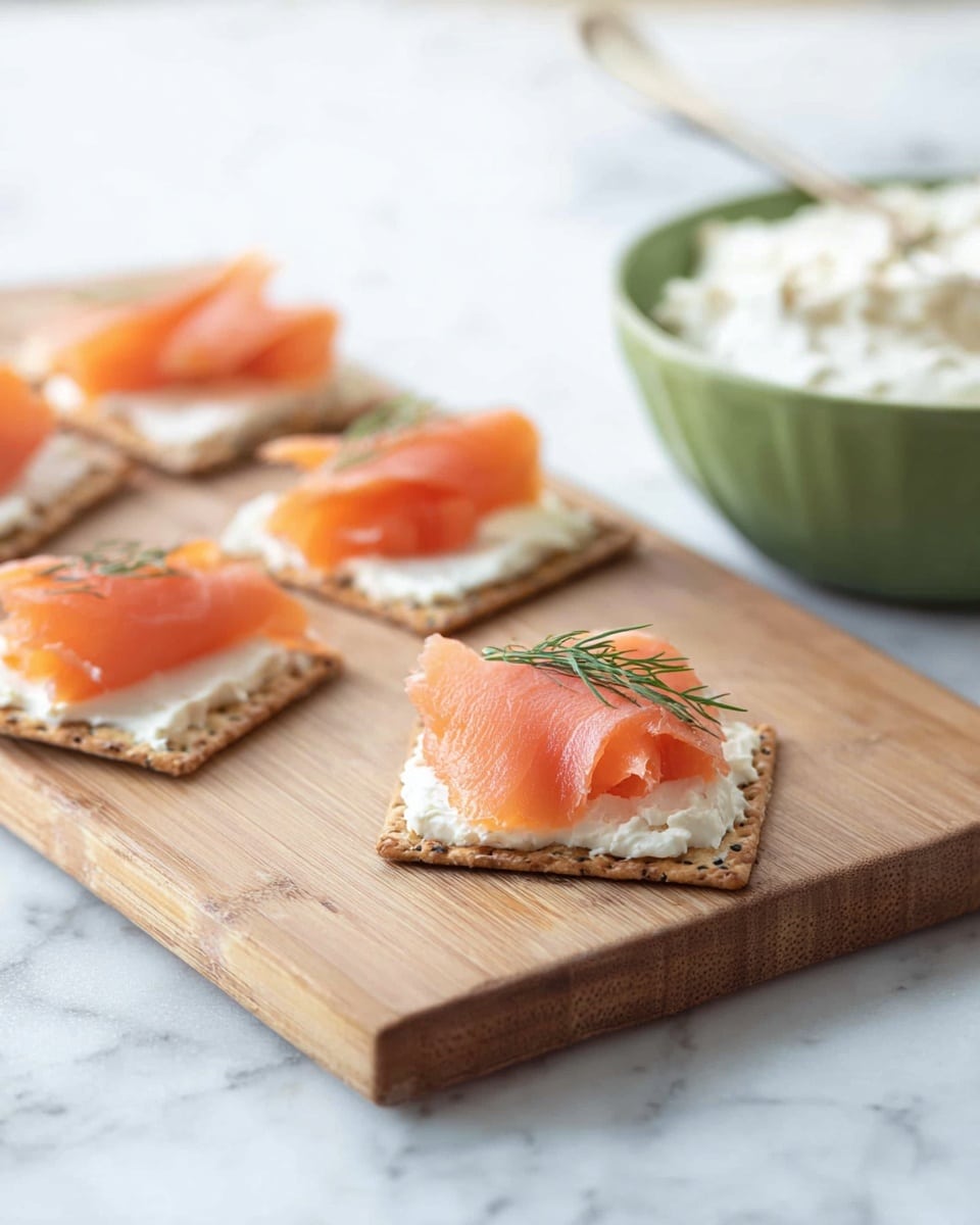 A woman's hand is spreading white creamy cheese with green and black specks on a square light brown cracker with a wooden-handled butter knife. There are several more light brown square crackers stacked around on a wooden cutting board. In the background, a white bowl with a speckled texture holds more of the white cheese, with a small green herb leaf on top. The surface is a white marbled texture. Photo taken with an iphone --ar 4:5 --v 7