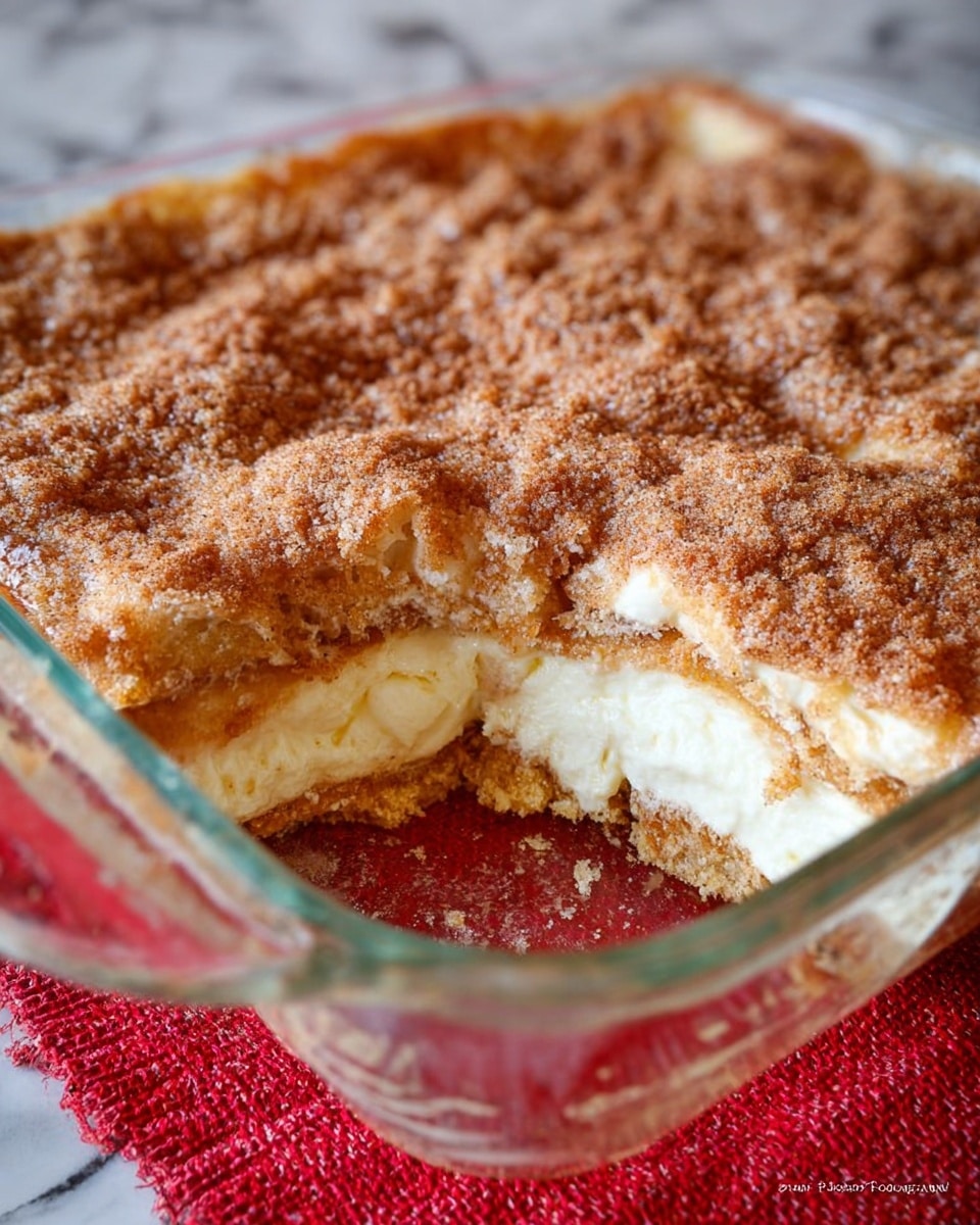 The image shows a clear square glass dish with three visible layers of dessert inside. The bottom layer is a light brown, crumbly crust. The middle layer is creamy white, smooth, and thick. The top layer is golden-brown with a rough, sugar-coated texture, uneven with some small darker spots. A portion of the dessert has been taken out from the front corner, revealing all three layers clearly. The dish is resting on a textured red cloth with a white marble surface in the background. photo taken with an iphone --ar 4:5 --v 7