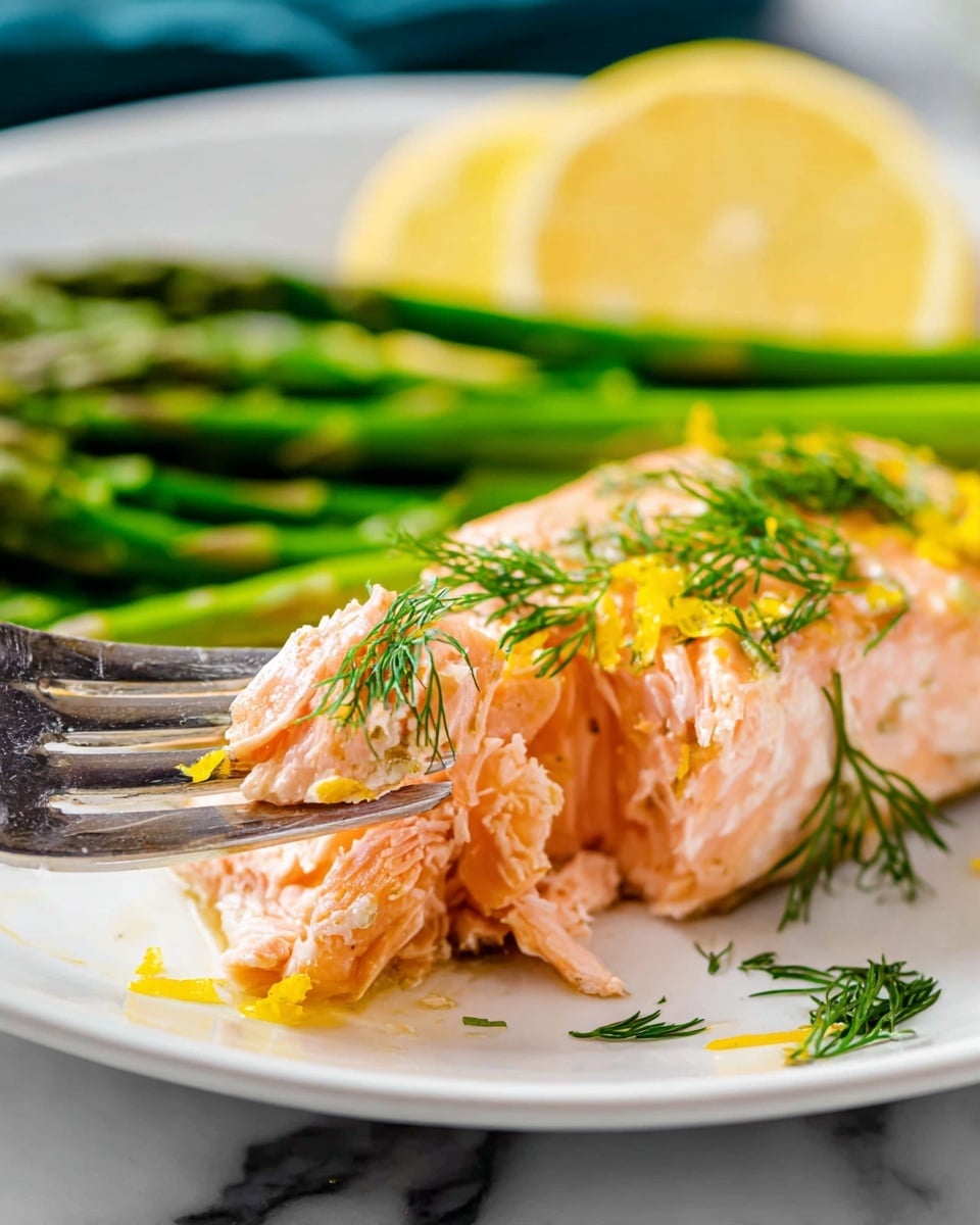 A white plate with a cooked pink salmon fillet in the foreground, topped with a few sprigs of fresh green dill and small yellow lemon zest pieces scattered on top and around it. A silver fork is pulling apart a piece of the salmon, showing its moist and soft texture inside. Behind the salmon, there are several vibrant green asparagus stalks, and a smooth yellow lemon wedge is placed towards the back. The plate sits on a white marbled surface. Photo taken with an iphone --ar 4:5 --v 7