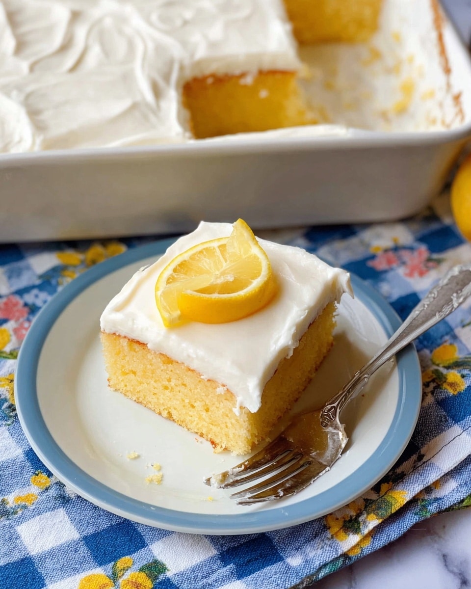 A square piece of lemon cake sits on a white plate, showing two layers: a soft yellow cake layer on the bottom and a thick smooth white frosting layer on top. The frosting covering the whole slice is creamy and white, with a small lemon wedge placed neatly in the center of the top. Next to the cake on the plate is a fork with traces of frosting. In the background, there is a white baking pan with more of the same lemon cake, with a large portion already taken out. The setting rests on a white marbled surface with a blue and white checkered cloth decorated with flower prints. Photo taken with an iphone --ar 4:5 --v 7