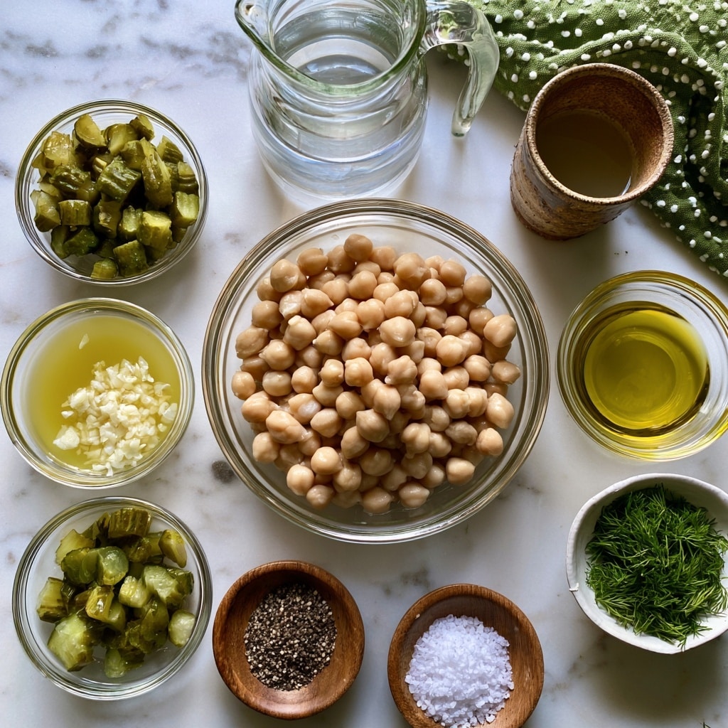The image shows various ingredients arranged neatly on a white marbled surface. At the center is a clear glass bowl filled with light beige chickpeas, surrounded by smaller clear glass bowls containing chopped green dill pickles, minced white garlic, yellow pickle juice, light yellow olive oil, and green fresh dill in a white bowl. There are also small wooden bowls holding black pepper and white salt. A clear glass pitcher holds water, and a rustic brown cup contains lemon juice. Near the top right corner, there is a green cloth with white dots. Each item is labeled in black text above or below the container. photo taken with an iphone --ar 4:5 --v 7