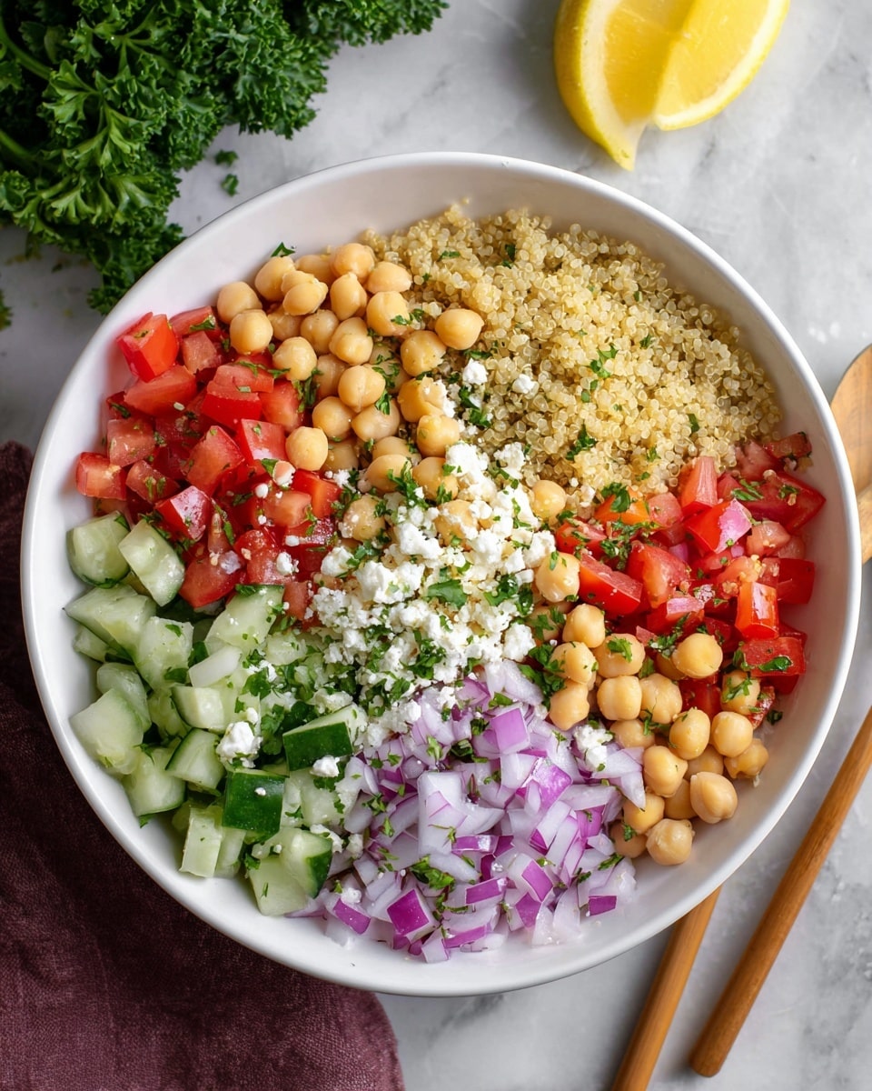 A white bowl filled with a base layer of light tan quinoa, topped in sections with bright beige chickpeas, small diced deep red tomatoes, finely chopped dark green parsley, crumbly white cheese, small diced purple onions, diced bright red bell peppers, diced light green cucumbers with some white pieces mixed in, and a single yellow lemon wedge placed on top near the cucumbers. The bowl is set on a white marbled surface with some green parsley visible in the background and wooden chopsticks placed beside the bowl. photo taken with an iphone --ar 4:5 --v 7