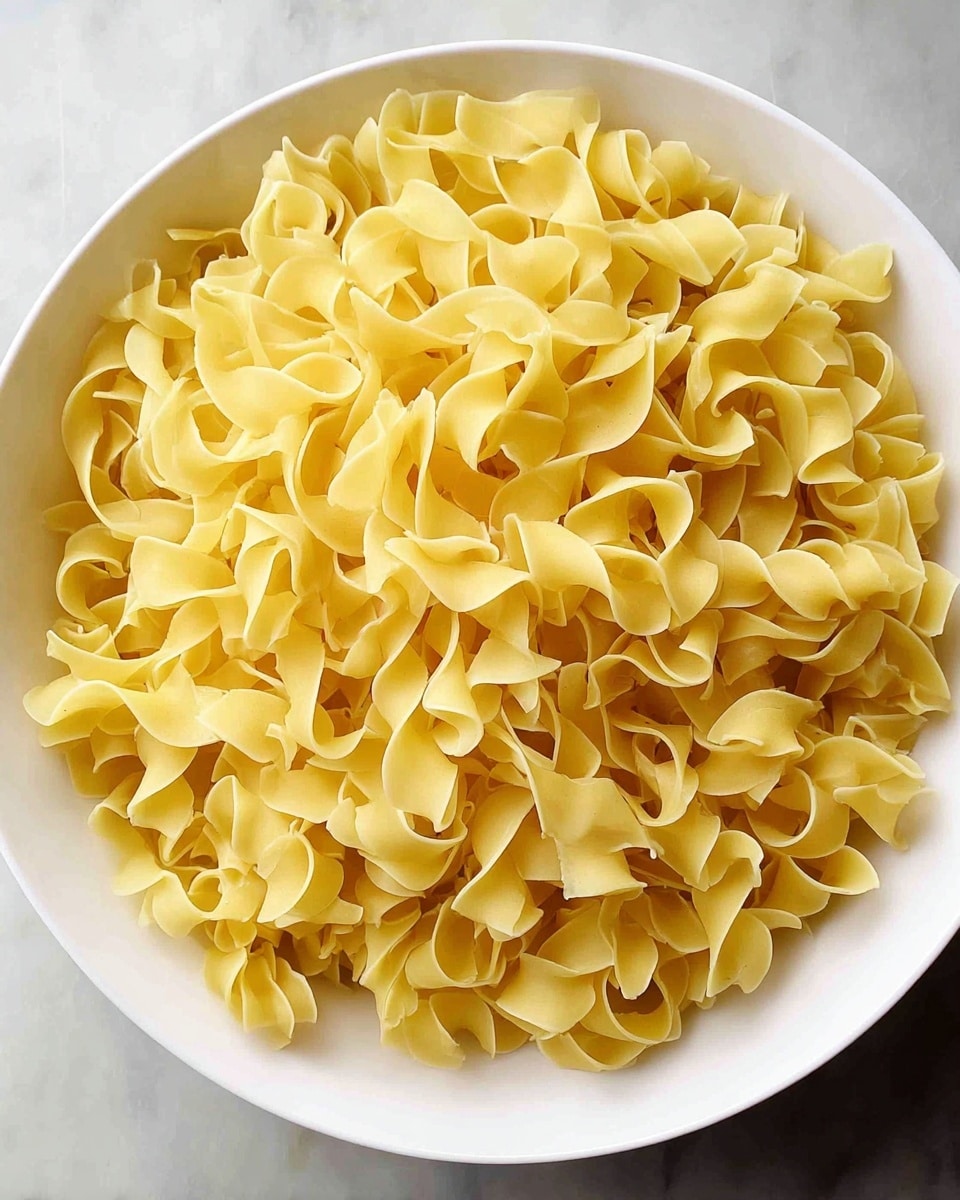 A white bowl filled with a large amount of uncooked yellow egg noodles, showing their curly and twisted shapes layered closely together. The bowl is placed on a white marbled surface. The noodles have a smooth and slightly rough texture, with some of them overlapping each other, creating a full and dense look. Photo taken with an iphone --ar 4:5 --v 7