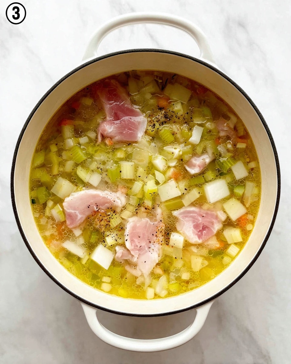 A white pot with two handles is filled with a yellow broth containing various ingredients. At the bottom and scattered throughout are small cubes of white and light yellow vegetables, mixed with a few pieces of light green celery. Floating on top are several raw light pink pieces of meat. The broth is clear but has a slightly oily texture with some bubbles and specks of black seasoning. The pot sits on a white marbled surface. photo taken with an iphone --ar 4:5 --v 7