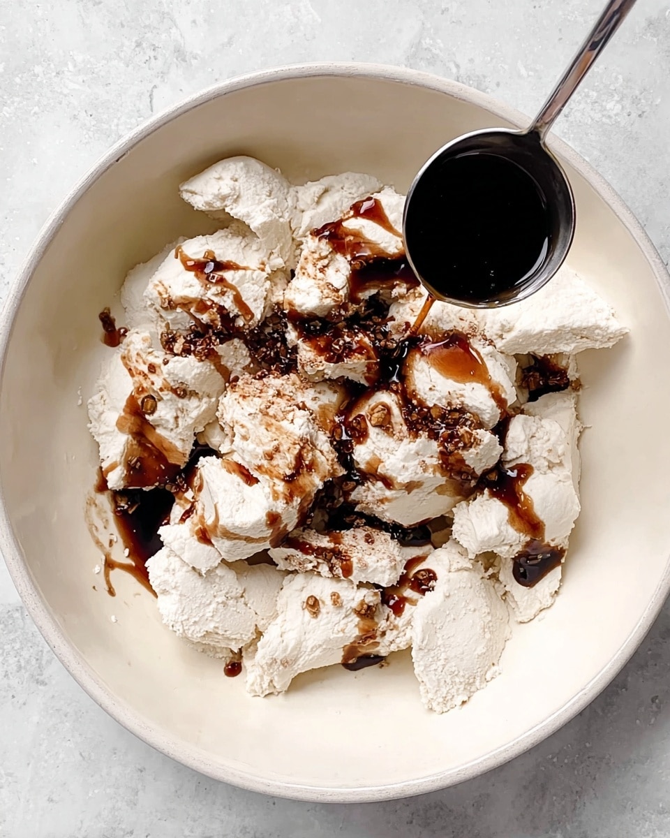 A large white bowl sits on a white marbled surface filled with chunks of soft white dough scattered unevenly. Dark brown syrup is drizzled over the dough, creating wet patches and drops around it. A silver measuring spoon filled with more dark syrup hovers above the bowl on the right side, about to add more. The dough pieces have a rough texture, and the syrup is glossy and thick, contrasting sharply with the matte white dough. Photo taken with an iphone --ar 4:5 --v 7